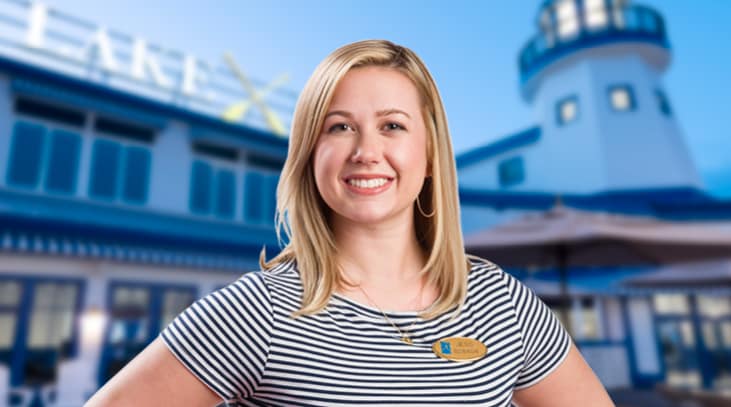 Seasonal team member smiling in a black and white striped shirt in front of the Lake House at Sylvan Beach